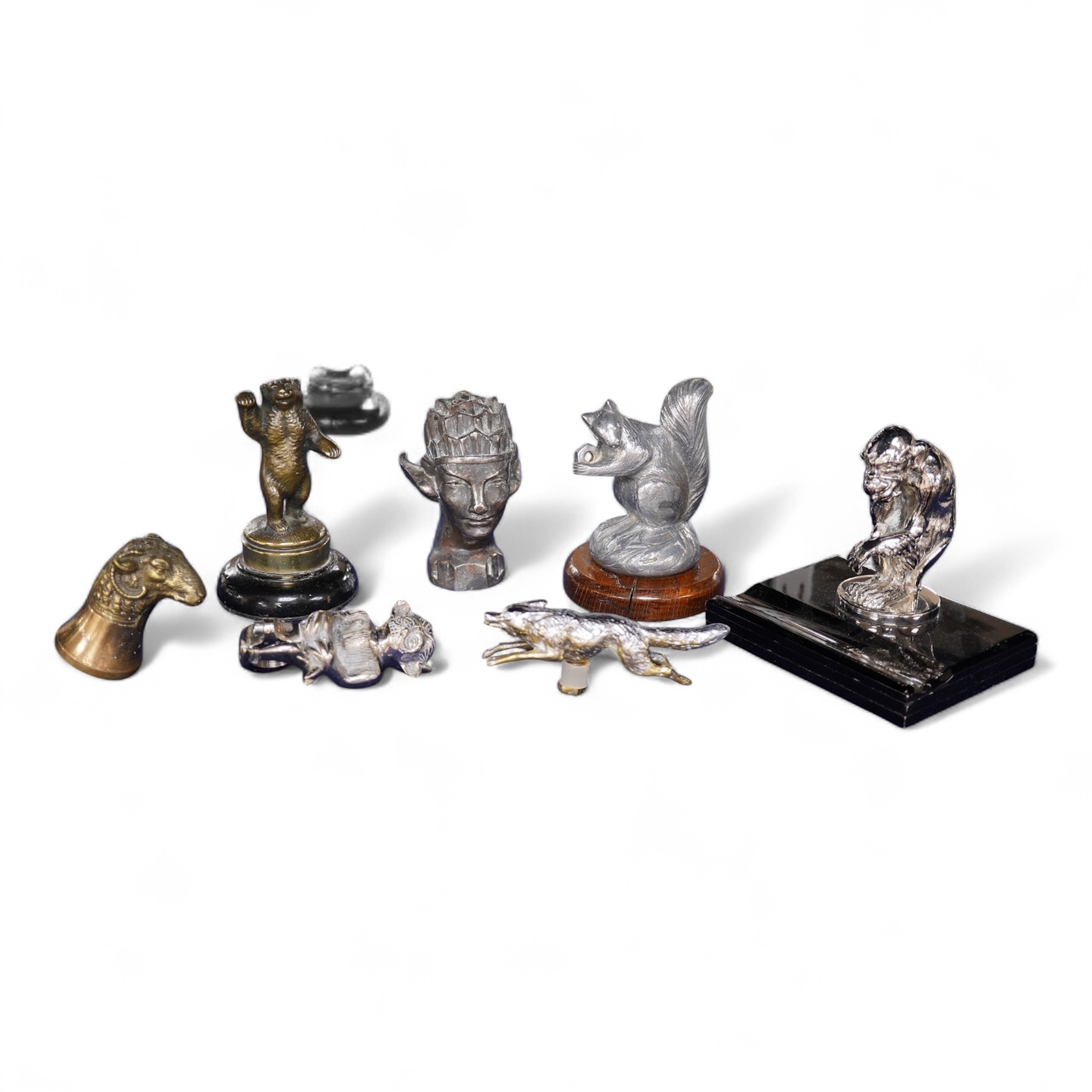 Seven chrome, brass and aluminium car mascots, etc. including an unusual and comical aluminium car mascot in the form of a squirrel holding a nut, together with a standing bear, an Art Deco winged head, a ram, a running